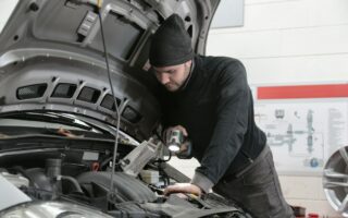 A mechanic inspects a car for used auto parts to sell.